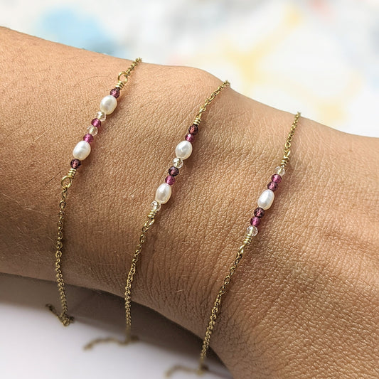 Three delicate gold chain bracelets with white baroque pearls and small pink gemstone accents, shown worn on a person's wrist.