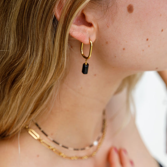 A person wearing a gold-toned necklace with a large black stone pendant and matching earrings.