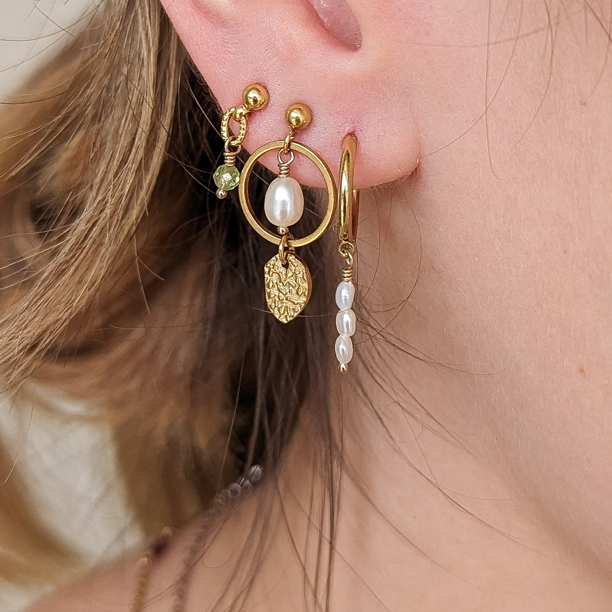 A person wearing a gold-toned hoop earring with multiple dangling elements, including what appears to be a birthstone.