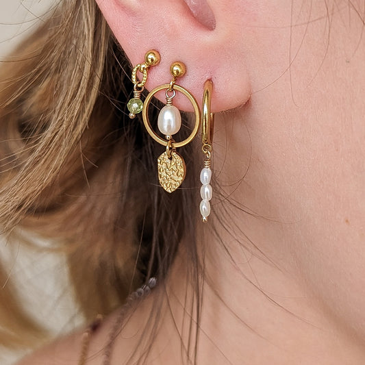 A person wearing a gold-toned hoop earring with multiple dangling elements, including what appears to be a birthstone.